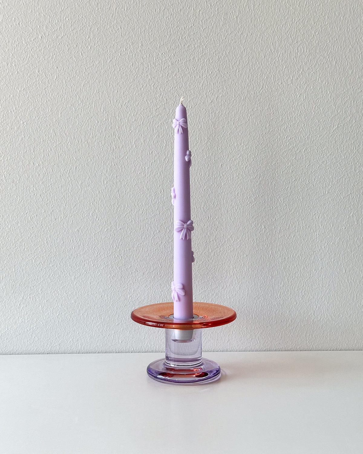 Lavender candle on a wooden and glass candle holder against a plain background