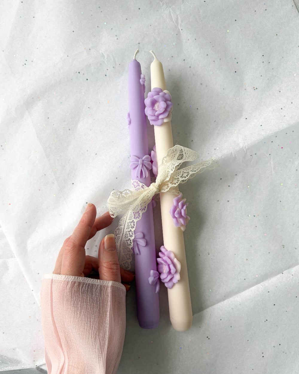 Decorative candles with floral designs held by a hand against a light background