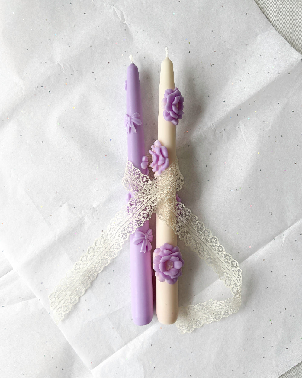 Two candles with floral decorations on a textured white surface