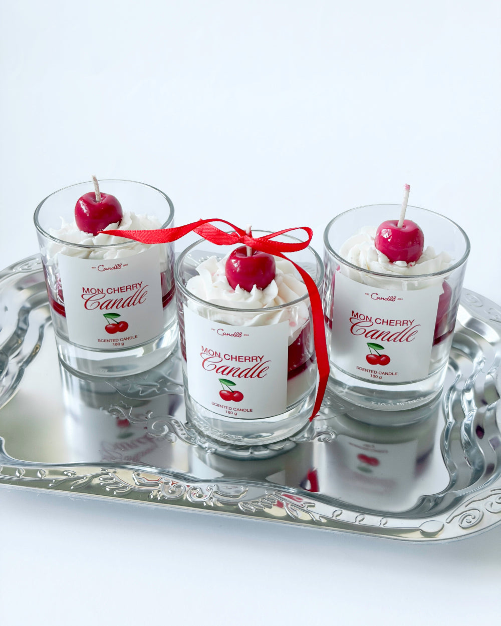 Three cherry-themed candles on a silver tray with a white background