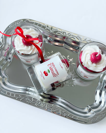 Silver tray with a bottle of cherry-flavored candle and two small containers of whipped cream with cherries on top.